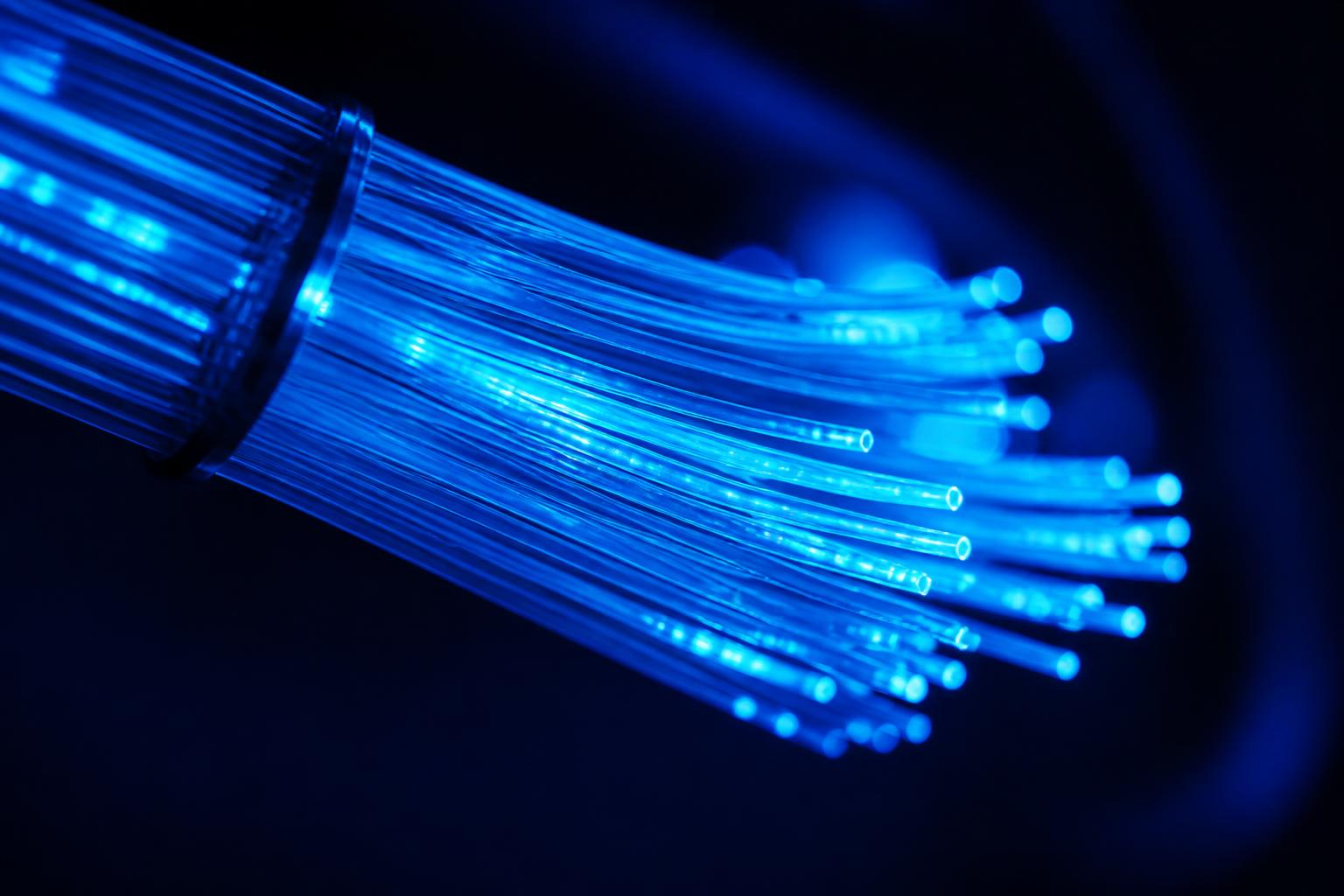 Primer plano de hilos de fibra óptica iluminados en tonos azul y cyan transmitiendo datos